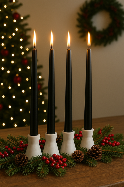 Four black candles in white holders on a wooden surface with Christmas decorations